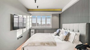 Een moderne slaapkamer met een groot bed, een aan de muur bevestigde televisie en een raam met uitzicht op de stad.