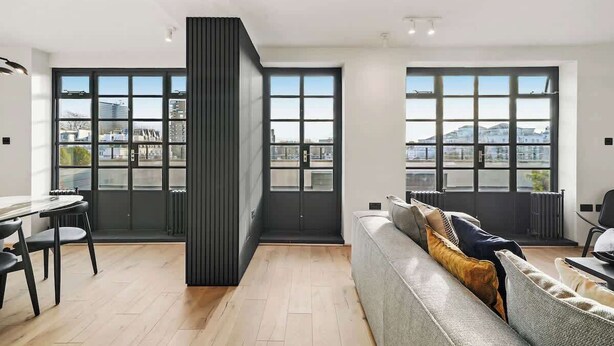 Een moderne woonkamer met een bank, een eettafel met stoelen en grote ramen met uitzicht op de stad.
