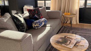 Een moderne woonkamer met een grijze bank, decoratieve kussens, een ronde salontafel en een getextureerd vloerkleed.