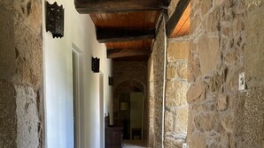 Un corredor de piedra con techo de madera, que conduce a una habitación con escritorio y silla.