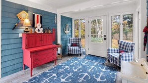 A room with a red dresser, two checkered armchairs, a blue and white patterned rug, and a door leading outside. - Game Room, Central AC, 4 mins to Craigville Beach! (Barnstable)