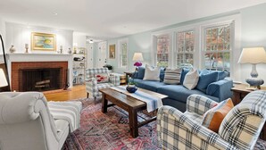 A living room with a fireplace, a blue sofa, plaid chairs, and a patterned rug. - Game Room, Central AC, 4 mins to Craigville Beach! (Barnstable)