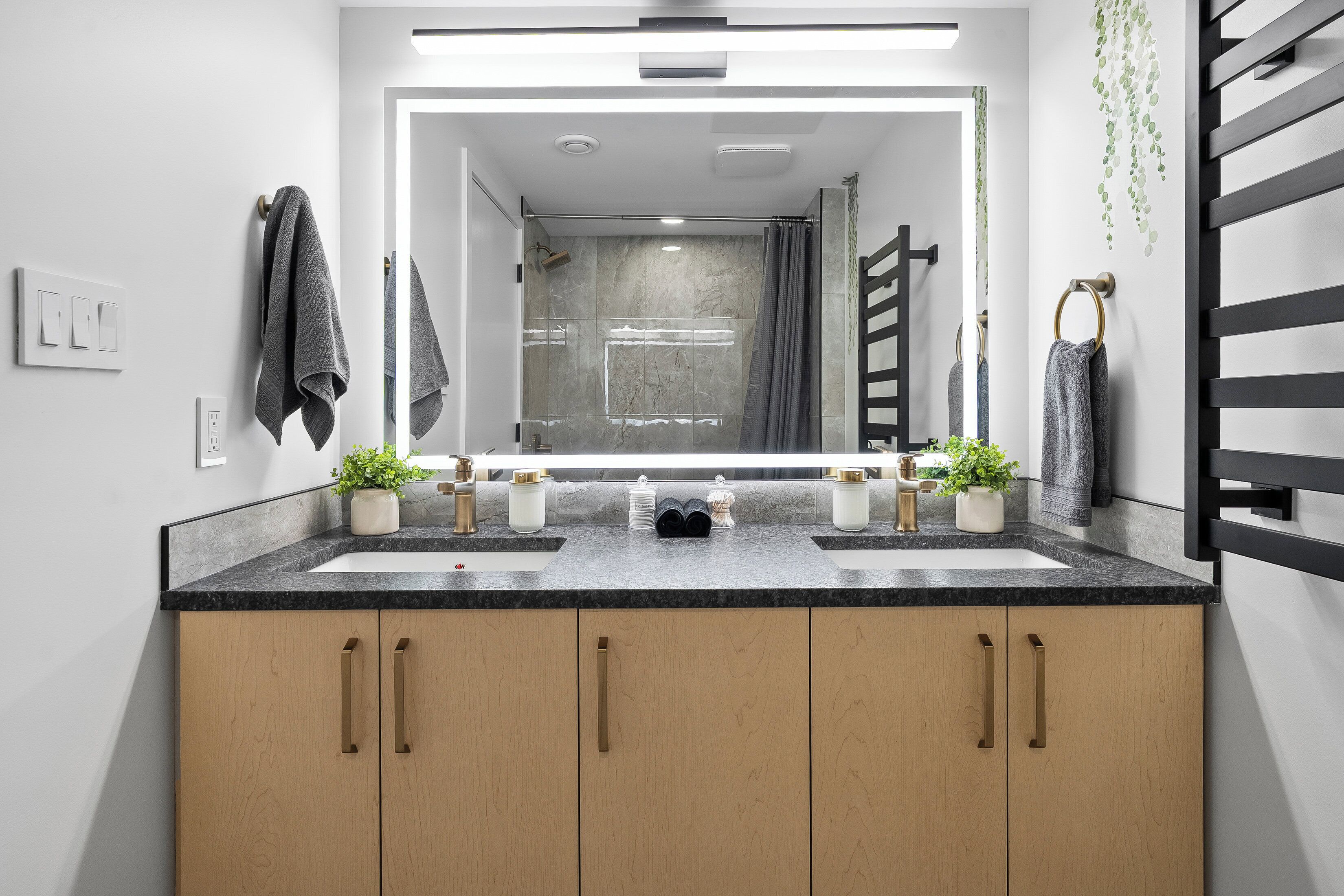 A modern bathroom with two sinks, wooden cabinets, and a large mirror.