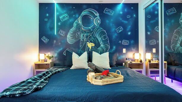 A bedroom with a large bed, a nightstand, a mirror, and a wall mural of an astronaut.