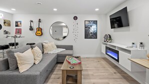 A modern living room with a grey sofa, a coffee table, a flat-screen TV, and a fireplace.
