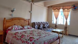 A bedroom with a wooden bed, a sofa, a small table, and a window with curtains. - Pereybere Beach Apartments: Studio with Balcony (Pereybere)