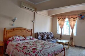 Ein Schlafzimmer mit einem hölzernen Bett, einem Sofa, einem kleinen Tisch und einem Fenster mit Vorhängen.