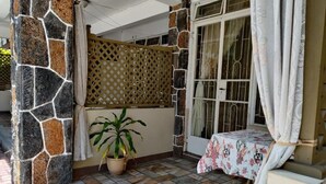 A covered outdoor area with stone walls, a potted plant, a table with a floral tablecloth, and a window with curtains. - Pereybere Beach Apartments: Studio with Balcony (Pereybere)