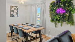 A dining area with a wooden table set for four, a chandelier, a wall-mounted plant wall, and a neon sign.