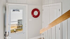 A hallway with a white door, a red circular object on the wall, and a staircase with a wooden handrail.