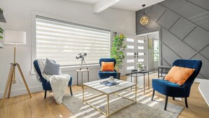 A modern living room with two blue armchairs, a white and gold coffee table, and a large window with blinds. - Perfect for families & groups seeking comfort, games & style in Edmonton (Edmonton)