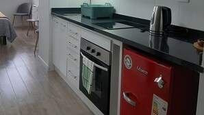Een kleine keuken met witte kastjes, een zwart aanrechtblad, een rode apparatuur en een raam met jaloezieën.