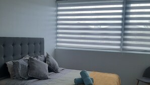 Een slaapkamer met een bed, kussens, een deken en een stoel.