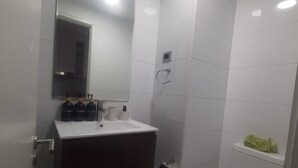 Een badkamer met een wit wastafel, spiegel, toilet en douche.