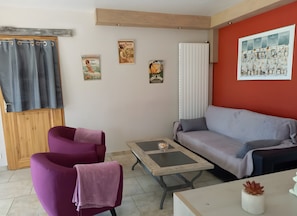 Un salon comprenant un canapé, deux fauteuils, une table basse et un mur orné de tableaux.