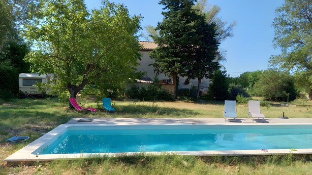 Piscina rectangular con solárium empedrado, rodeada de césped y árboles.