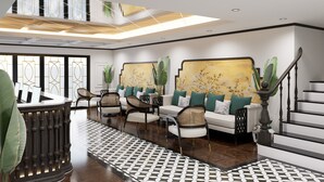 A spacious lobby with a high ceiling, a central seating area with sofas and chairs, a reception desk, and a staircase. - Halora Nova Cruise (Tuan Chau)
