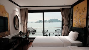 A hotel room with two beds, a desk, a chair, a TV, and a large window with a view of the sea and islands. - Halora Nova Cruise (Tuan Chau)
