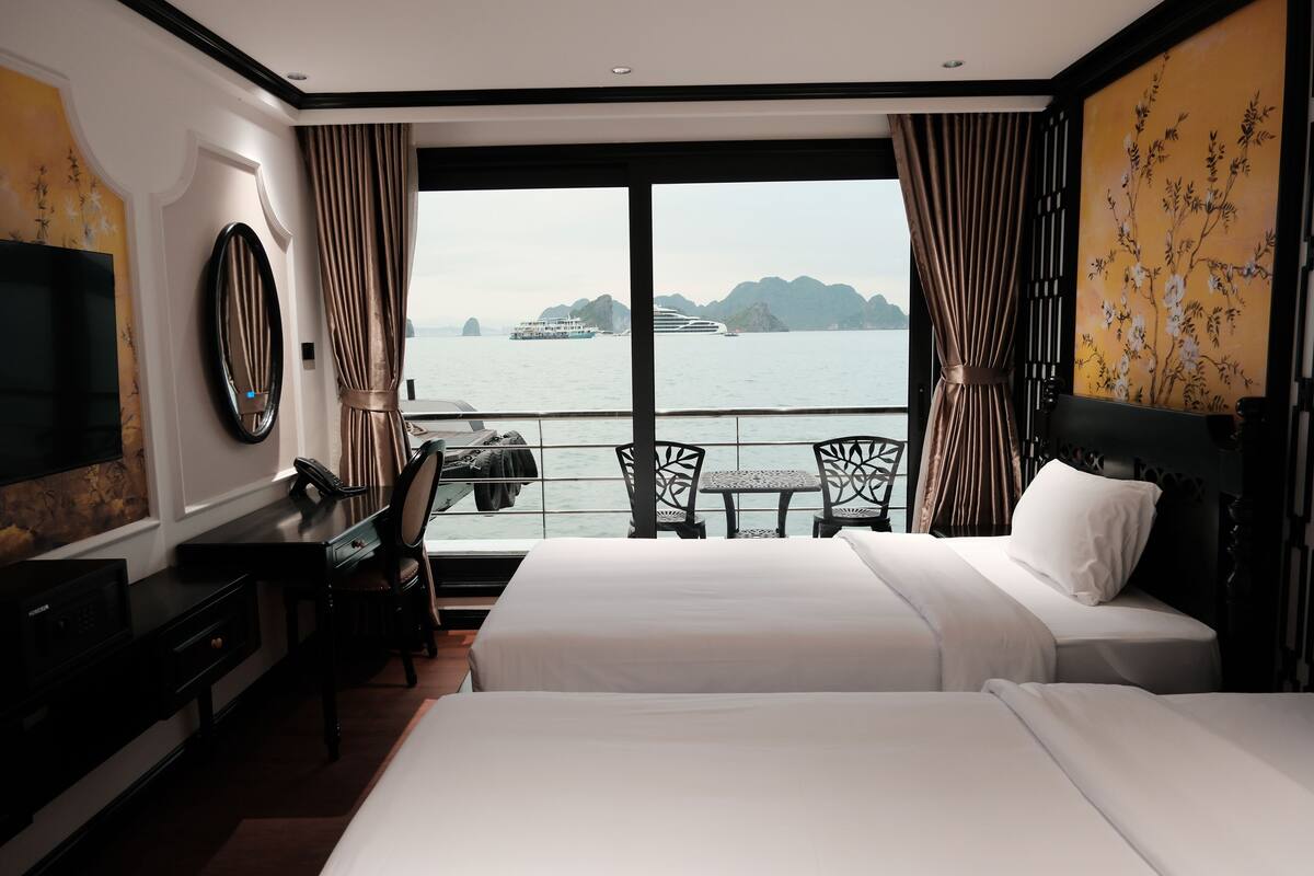 Habitación de hotel con dos camas, un escritorio, una silla, un televisor y un amplio ventanal con vistas al mar y a las islas.