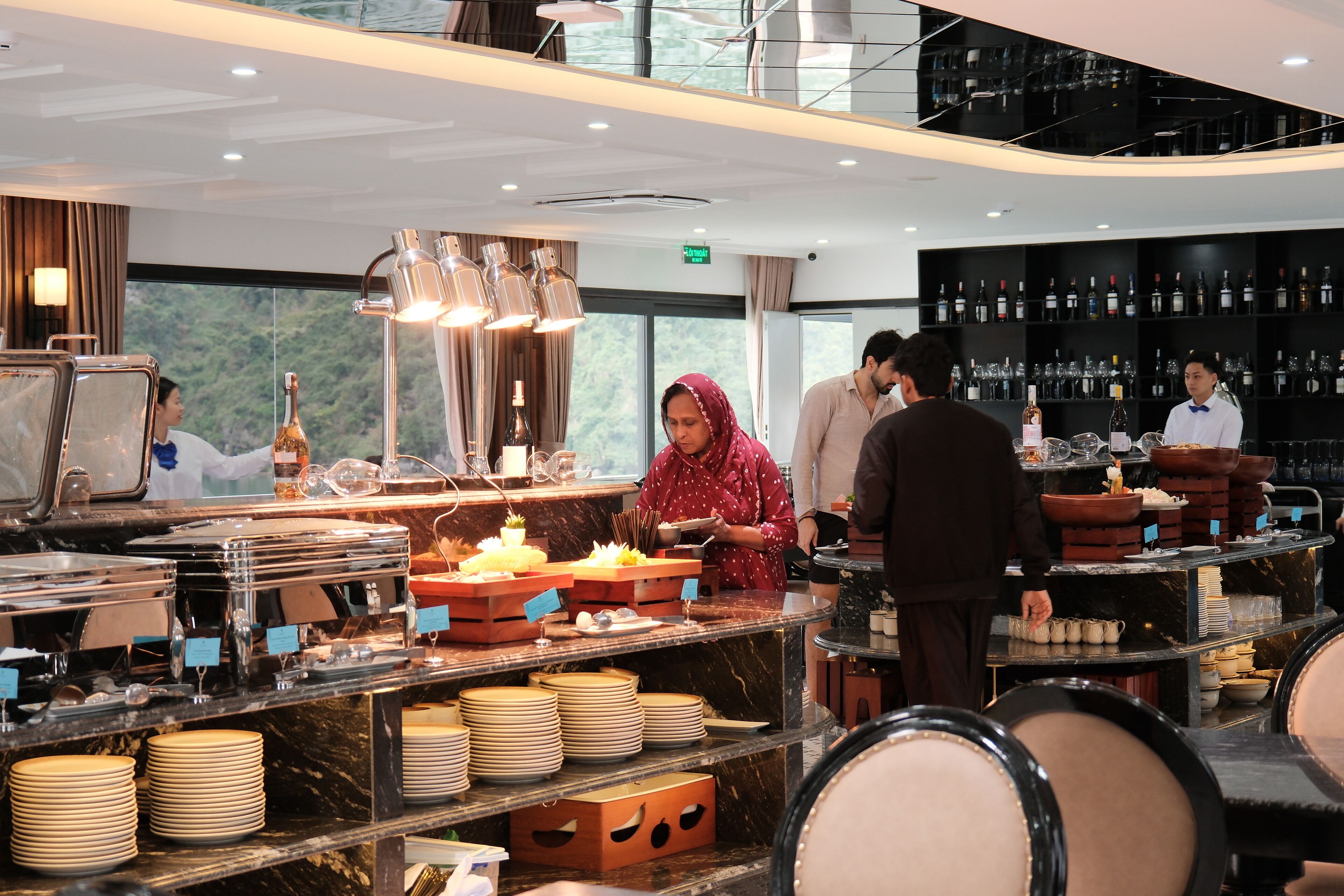 A hotel restaurant with a buffet setup, bar area, and wine racks.