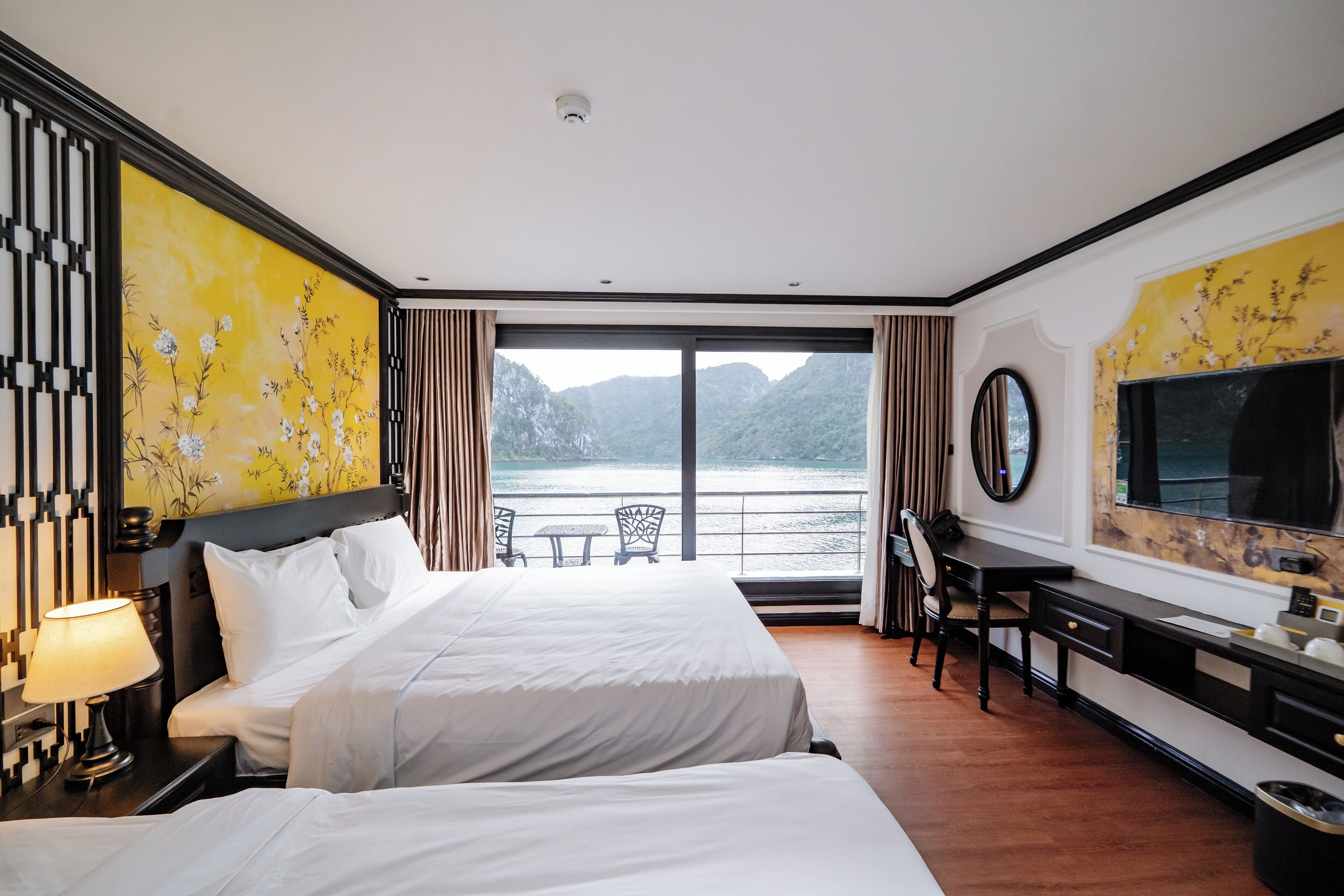 A hotel room with two beds, a desk, a chair, a TV, and a view of a body of water.