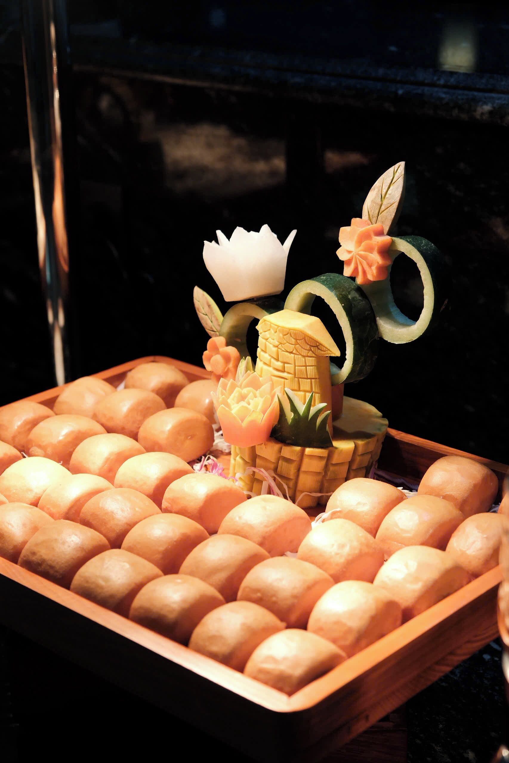 A tray of round, golden-brown baked goods with a decorative item resembling a small house with a crown and flowers.