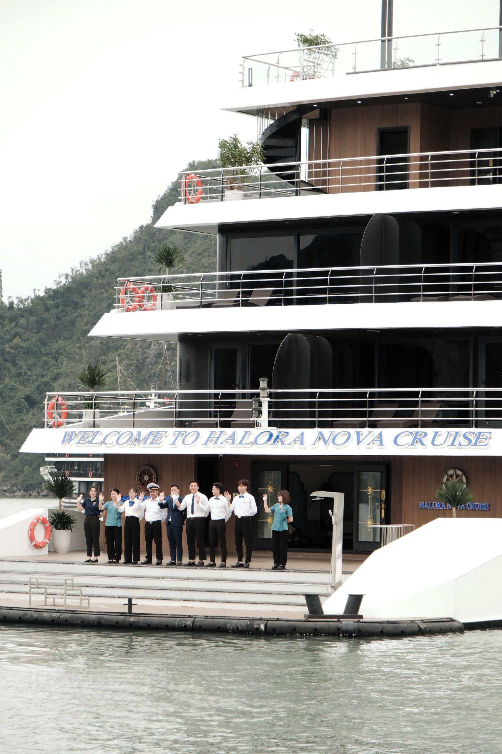 A multi-level cruise ship with a 'Welcome to Halona Nova Cruise' sign, lifebuoys, and a group of people standing on the deck.