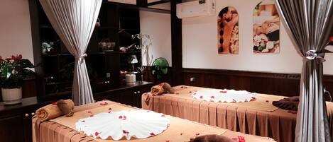 A room with two beds, each with a beige bedspread and white decorative pillows, a wooden cabinet, and a wall-mounted air conditioner.