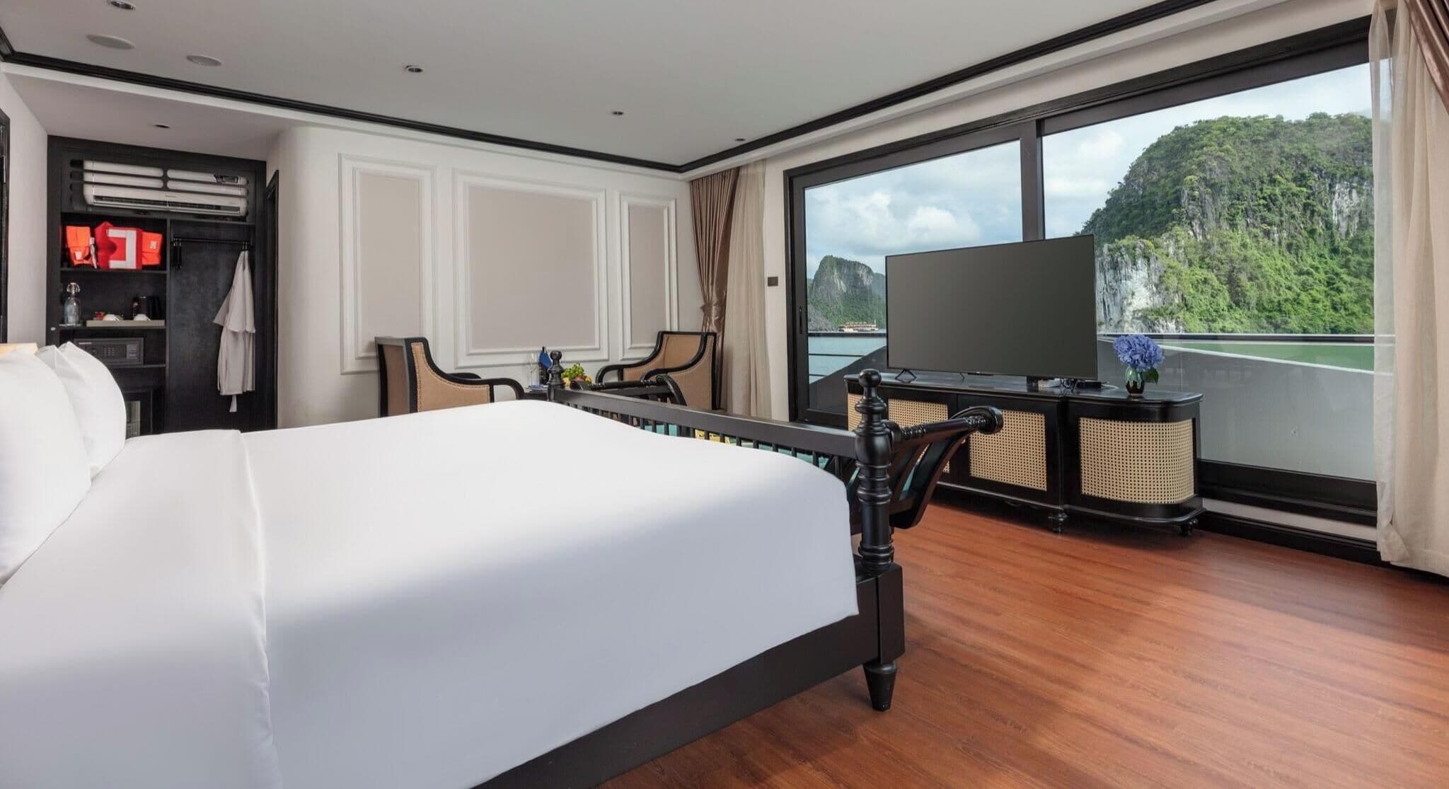 Habitación de hotel con una cama grande, televisión, escritorio con computadora y vista a un paisaje montañoso.