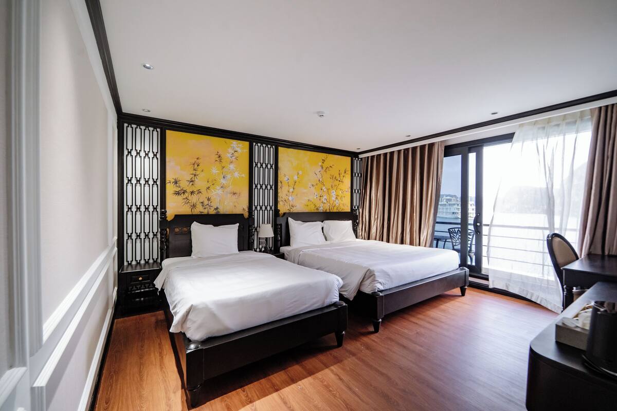 Habitación de hotel con dos camas, un escritorio, una silla y un ventanal con cortinas.