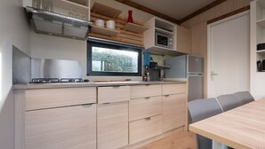 Cocina moderna con estufa integrada, microondas y refrigerador. Una ventana ofrece luz natural y vistas al verdor exterior.