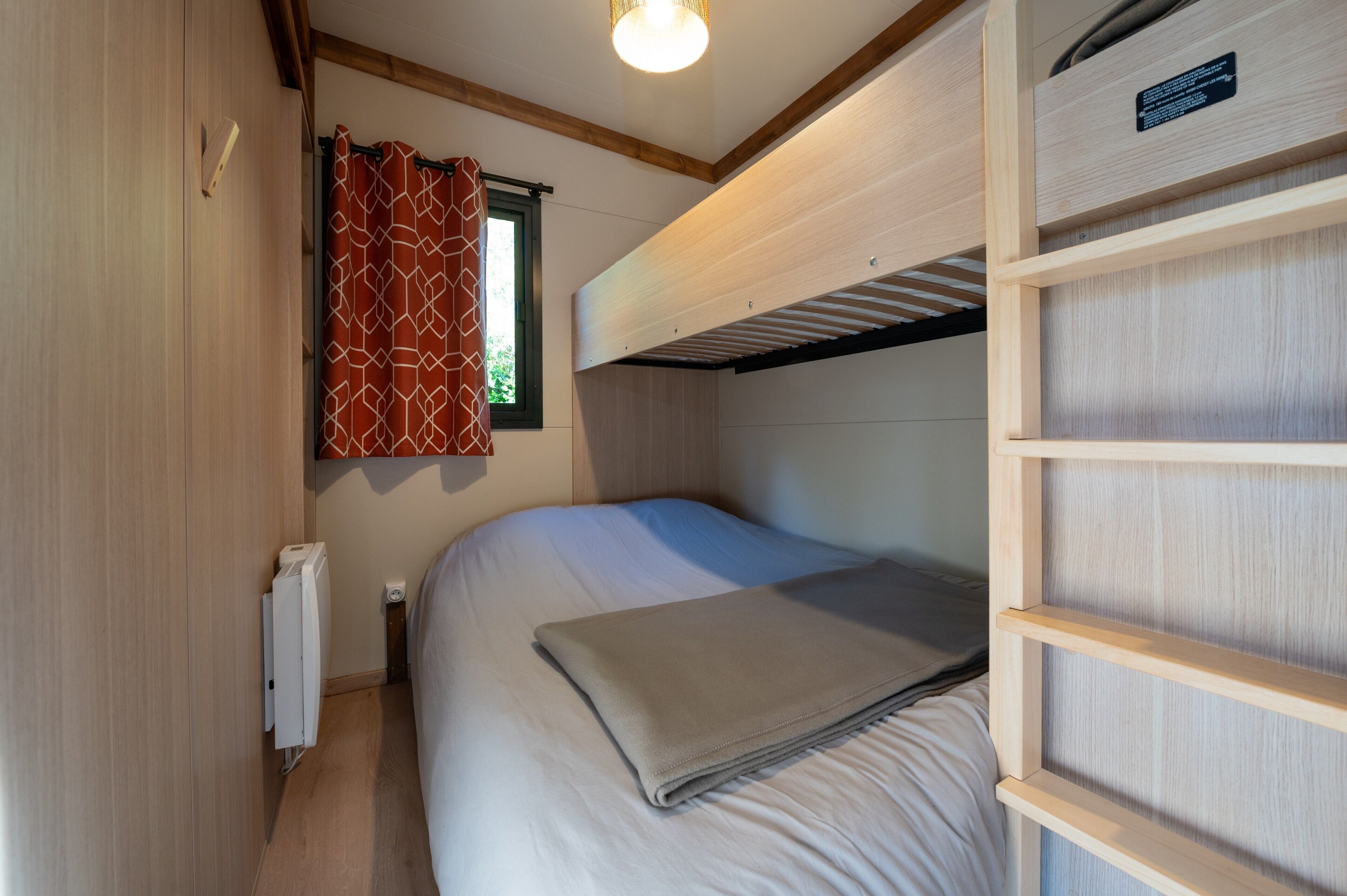 Ein kleines Zimmer mit einer Etagenbett, einem Fenster mit Vorhängen, einem Heizkörper und einem Regal mit einem Schild.