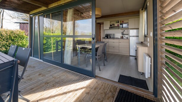 Une cuisine moderne dotée de portes coulissantes en verre qui donnent sur un espace extérieur avec une terrasse en bois et une table à manger.