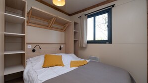 Une chambre à coucher comprenant un lit, des étagères intégrées, une fenêtre et un luminaire au plafond.