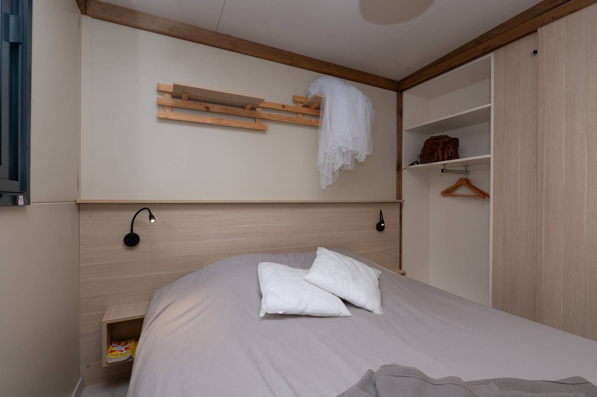 Une chambre à coucher comprenant un lit, une table de chevet, une étagère suspendue, une armoire et un luminaire fixé au mur.