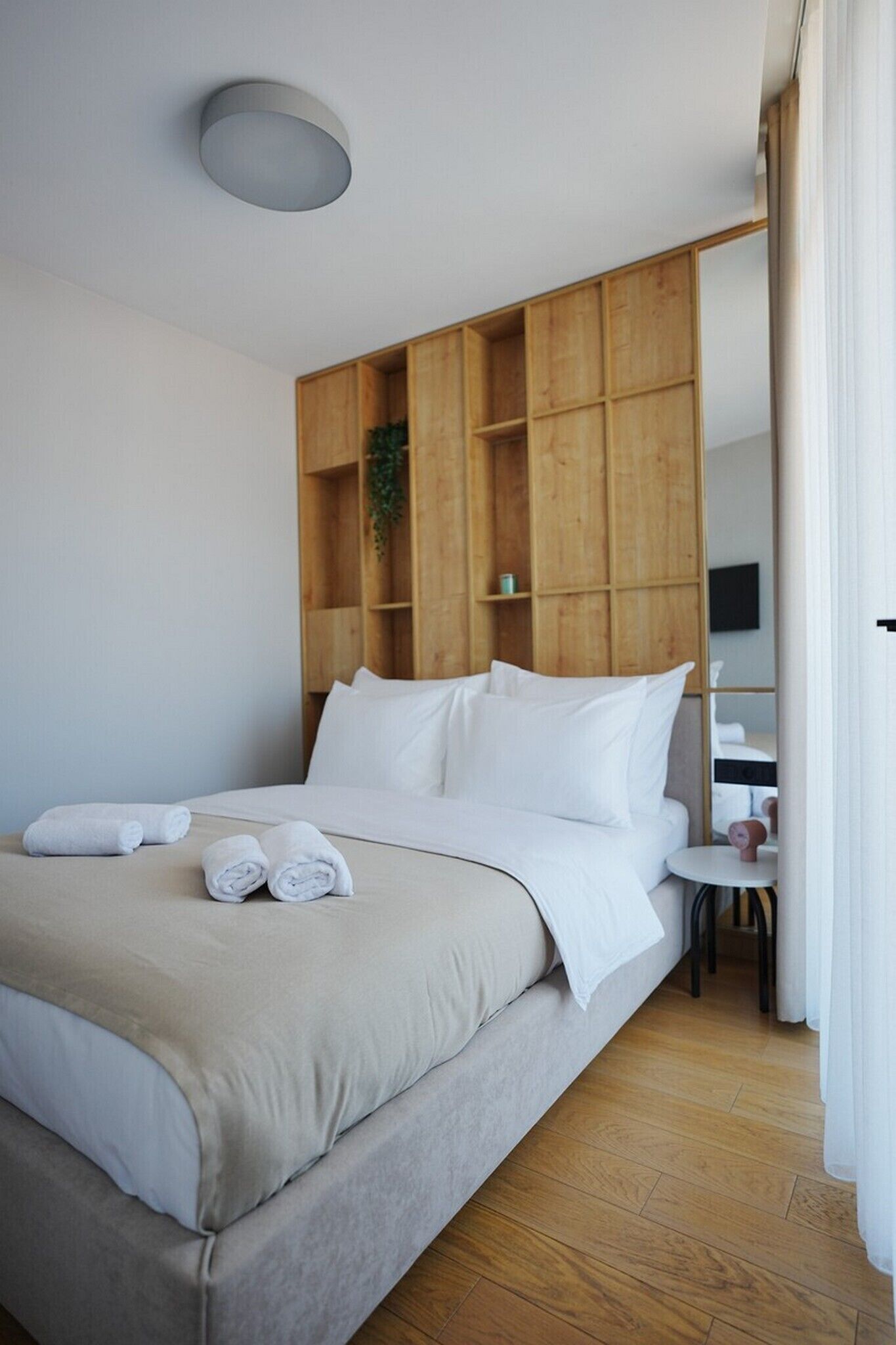 Een moderne hotelkamer met een bed, houten lambrisering, een klein bureau en een spiegel.