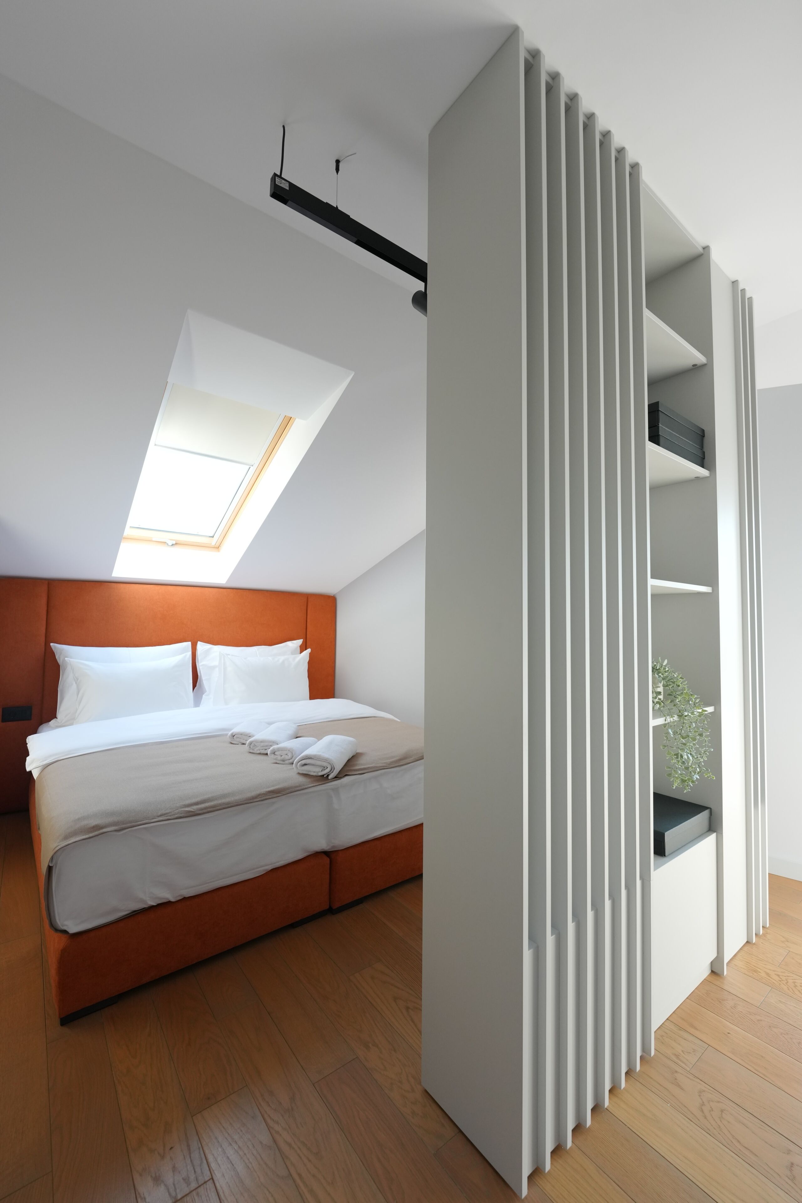 A modern bedroom with a bed, a skylight, and a white partition with shelves.