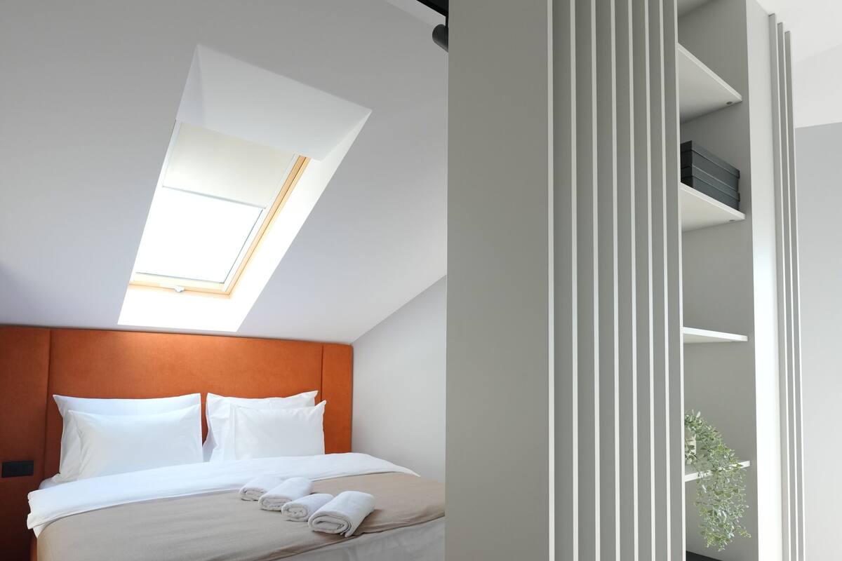 Un dormitorio moderno con cama, tragaluz y una pared divisoria blanca con estanterías.