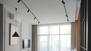 A modern hotel room with a wooden floor, a sofa, a desk with a chair, a TV, and a large window with curtains.
