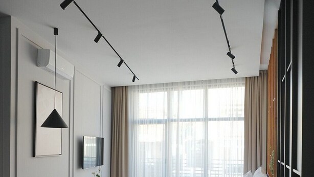 A modern hotel room with a wooden floor, a sofa, a desk with a chair, a TV, and a large window with curtains. - Madera (Čačak)