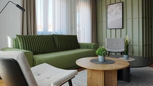 A modern living room with a green sofa, a round wooden coffee table, and a grey armchair. - Madera (Čačak)