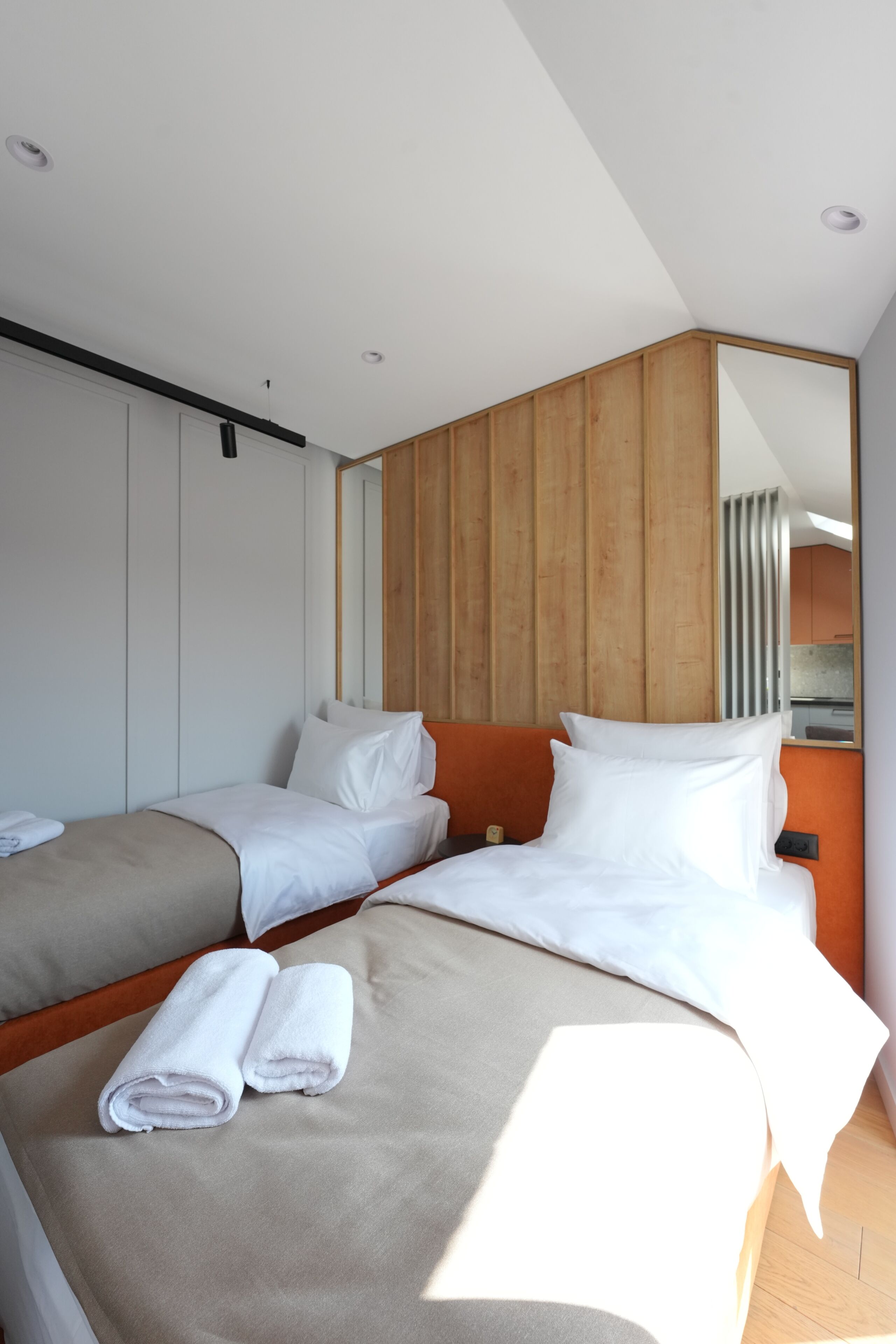 A modern hotel room with two beds, a large mirror, and a wooden accent wall.
