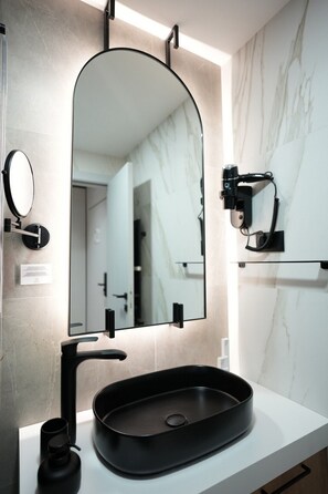 A modern bathroom with a black sink, a large mirror, and a camera mounted on the wall.