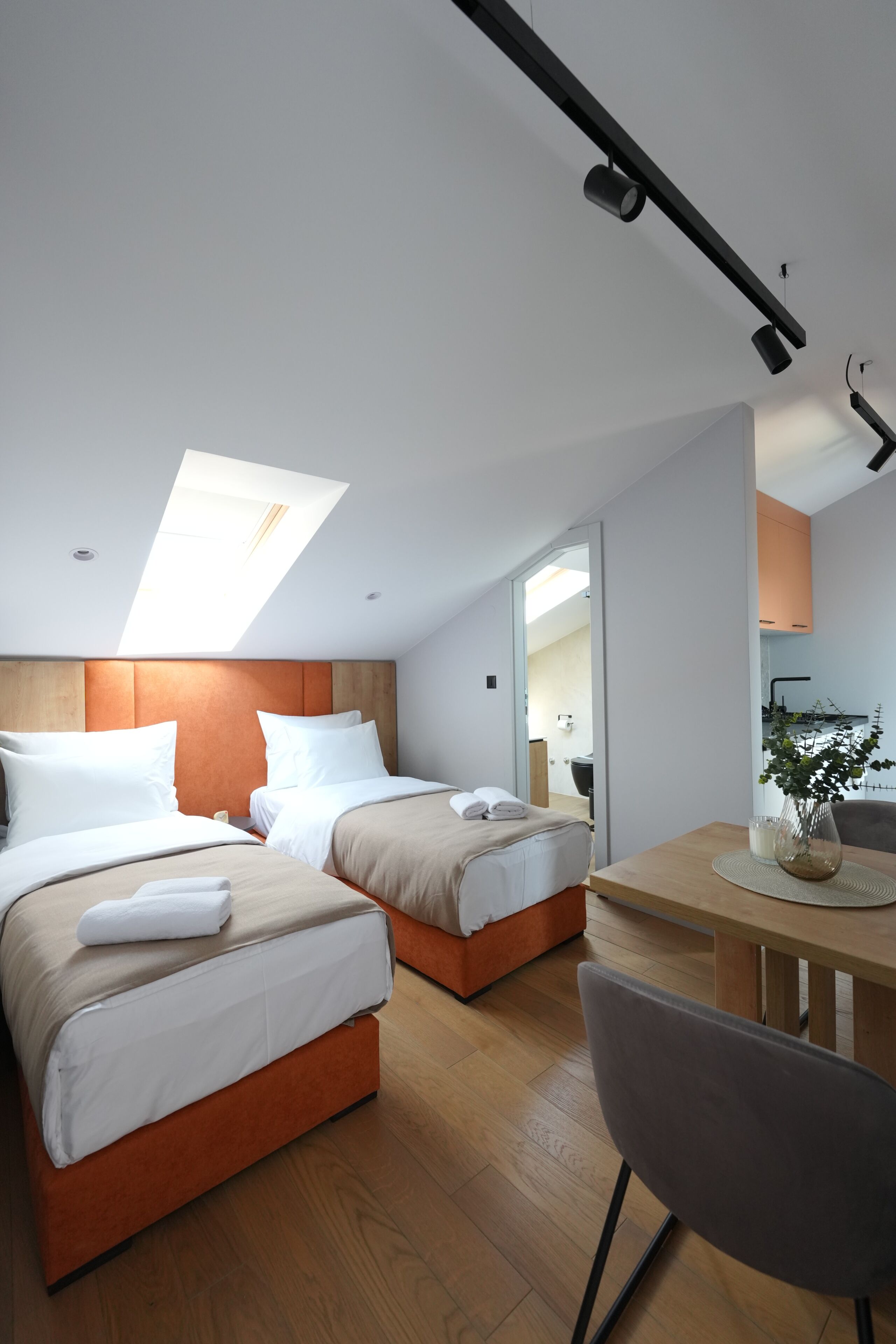 A modern hotel room with two beds, a dining table, and a kitchenette.