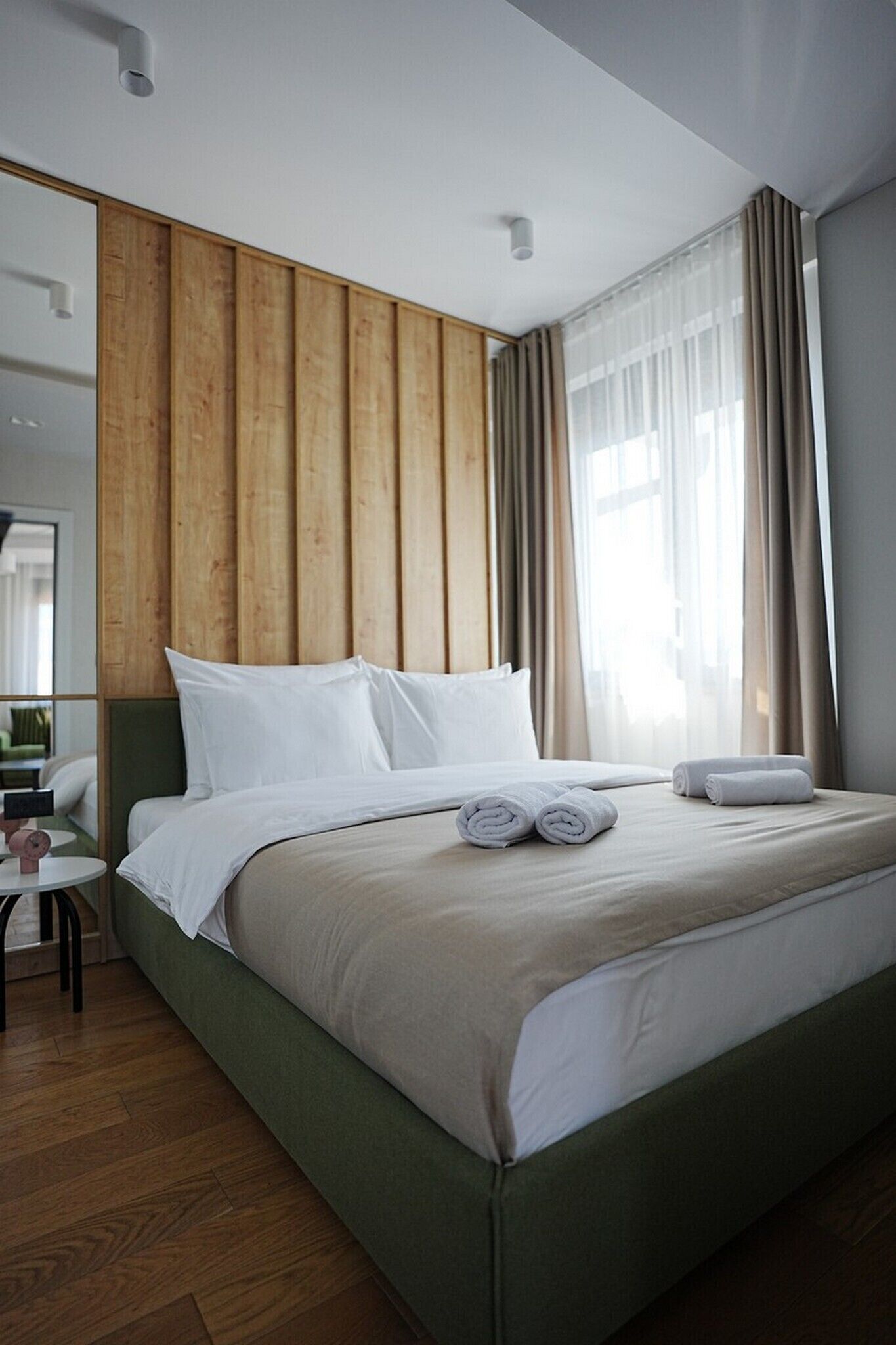 Ein Hotelzimmer mit einem großen Bett, einer Wand aus Holzpaneelen und Blick auf die Stadt durch transparente Vorhänge.