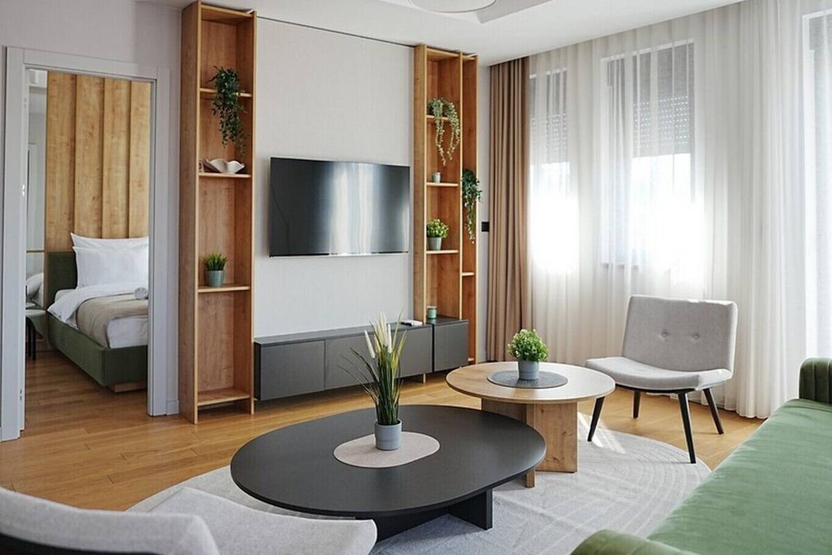 Una sala de estar moderna con televisor de pantalla plana, estanterías de madera, una mesa redonda de centro y un sofá verde.