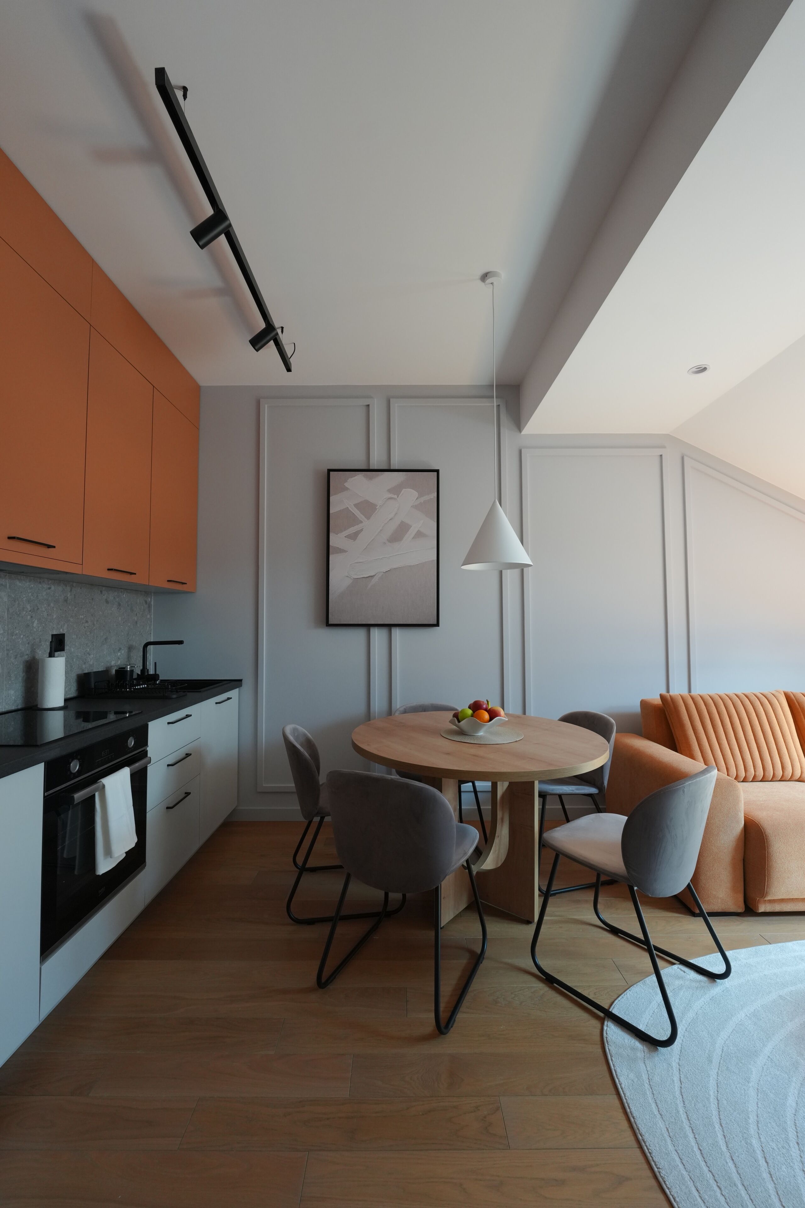 A modern kitchen with a dining area, featuring a wooden table, chairs, and a sofa with orange cushions.