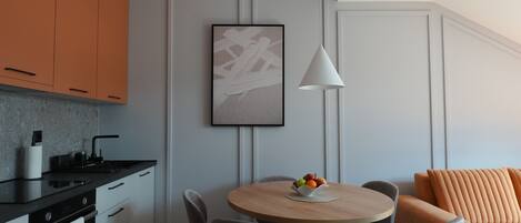 Una cocina moderna con zona de comedor, que incluye una mesa de madera, sillas y un sofá con cojines naranjas.