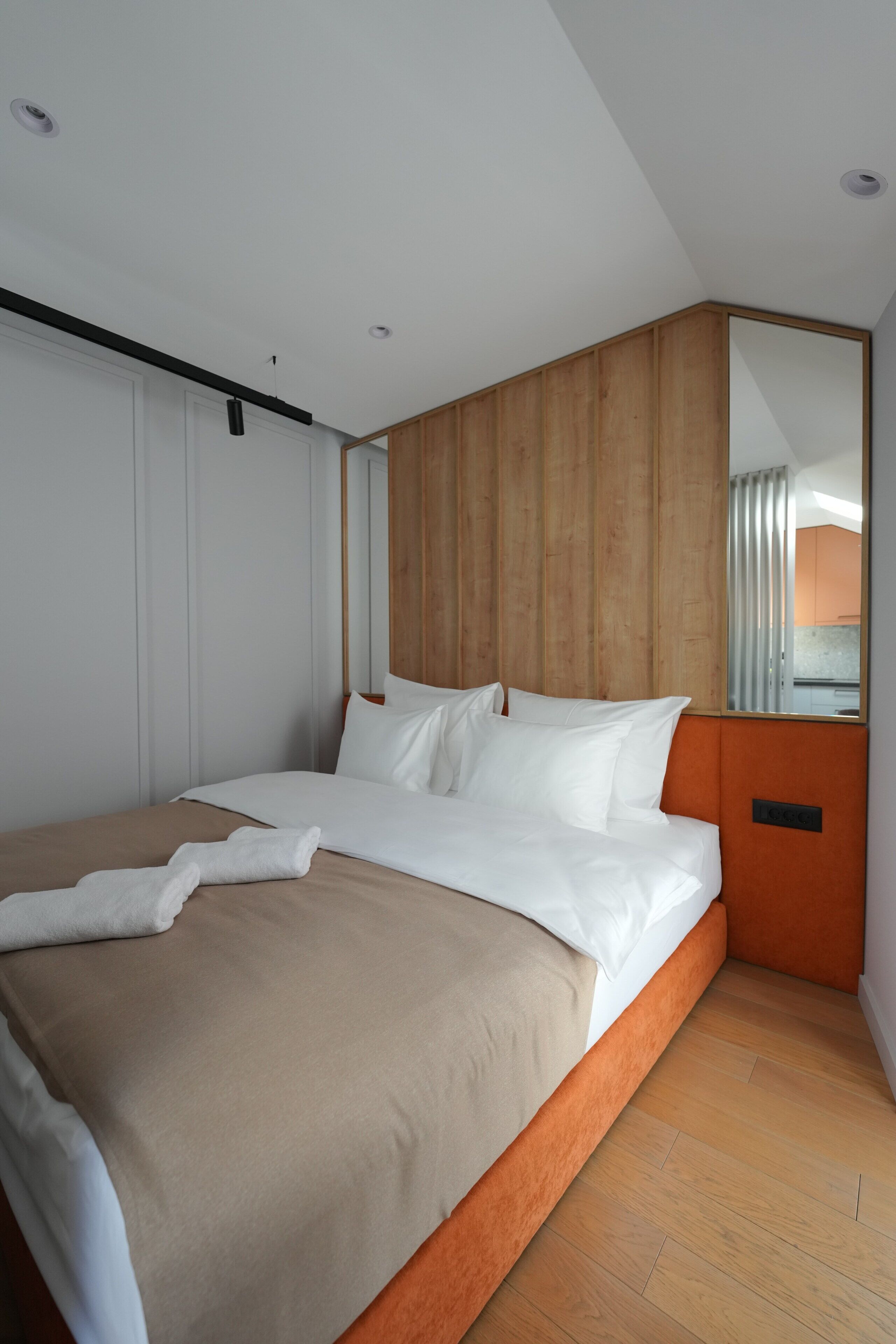 A modern hotel room with a large bed, wooden headboard, and a mirror reflecting the room.