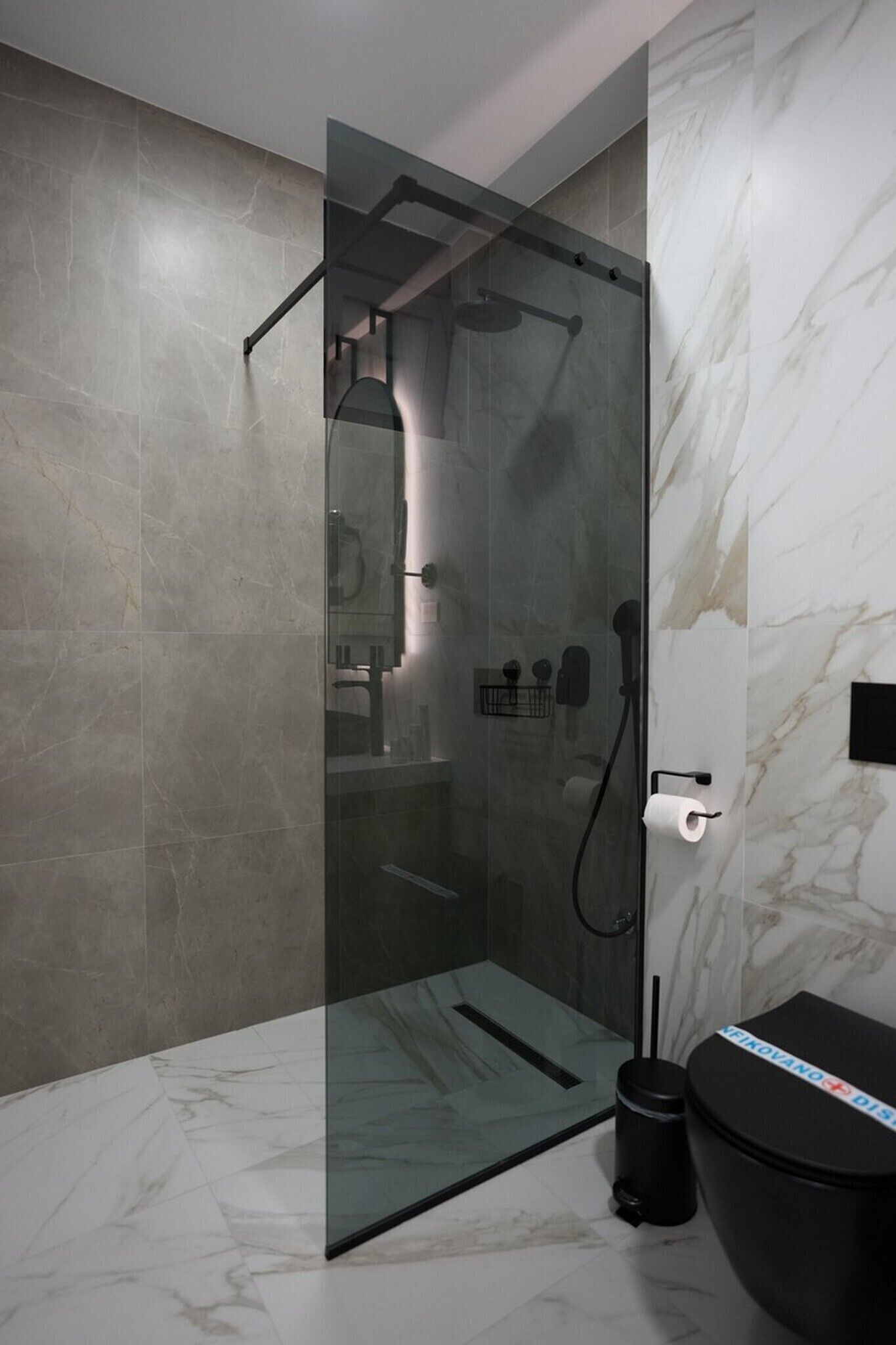A modern bathroom with a glass-enclosed shower, marble walls, and a black toilet.